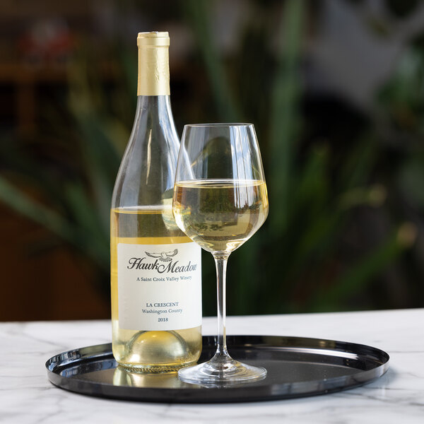A bottle of white wine and a filled wine glass are placed on a round, glossy black serving tray atop a marble surface.