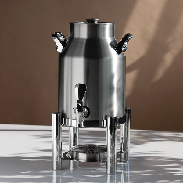 A stainless steel beverage urn with a spigot, two side handles, and a lid, elevated on a matching metal stand.