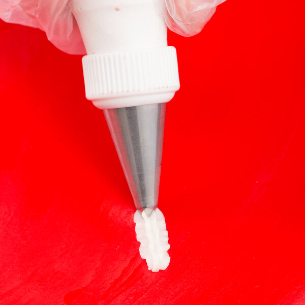 A close-up of a piping bag with a metal star-shaped tip dispensing white icing onto a red surface.