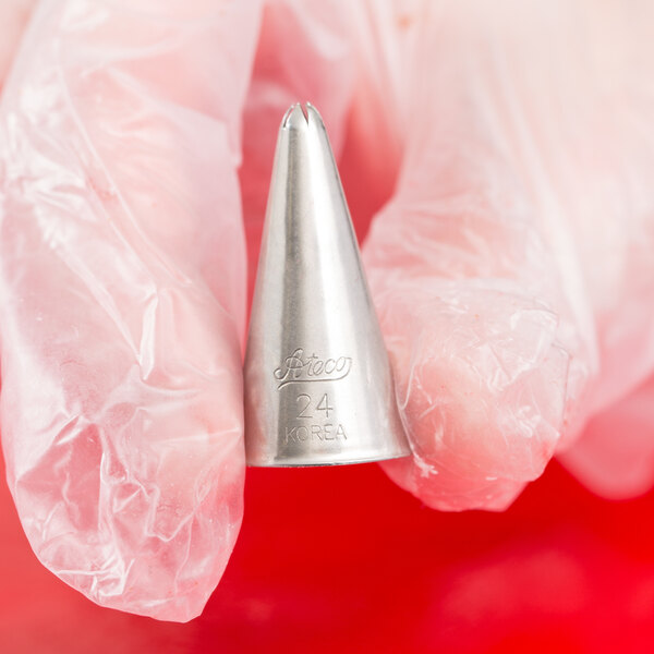 A person wearing a clear glove is holding a metal piping tip with a closed star opening.