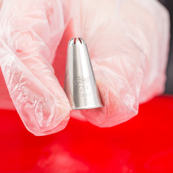 A gloved hand is holding a metal piping tip with a closed star-shaped opening.