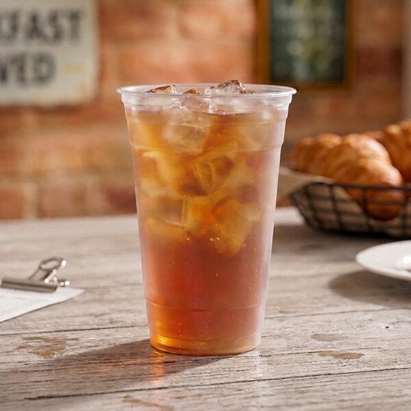 A clear plastic cup filled with iced tea and ice cubes, placed on a wooden table.