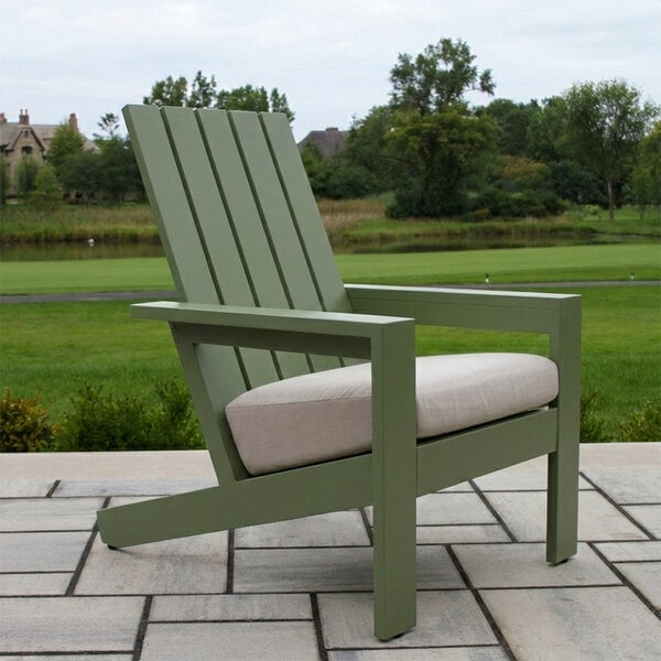 A green slatted outdoor chair with a beige cushion, placed on a patio with a grassy landscape in the background.