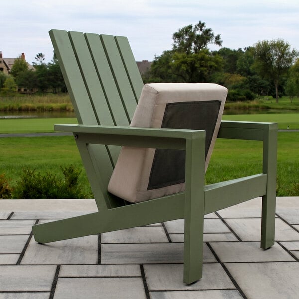 A green slatted Adirondack chair with a beige and gray cushion on a stone patio, set against a grassy outdoor landscape.
