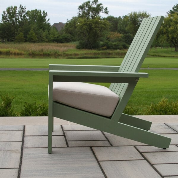 A green outdoor chair with a slatted back and a light-colored cushion, placed on a tiled patio with a grassy landscape in the background.