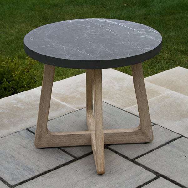 A round table with a dark, marble-like top and light wooden legs, placed outdoors on a stone patio.