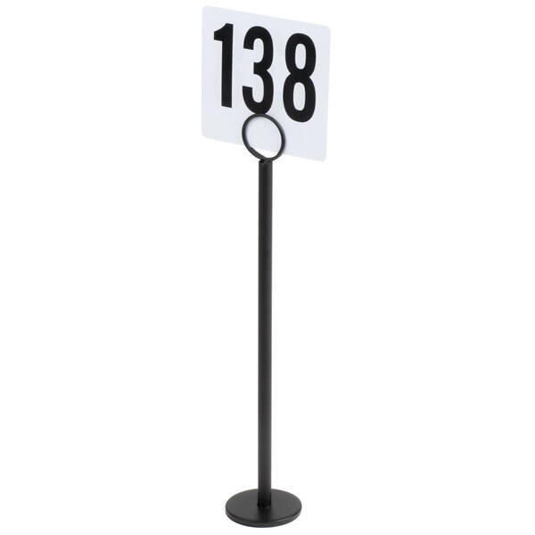 A tall black stand with a circular base holding a white card displaying the number 138 in bold black digits.