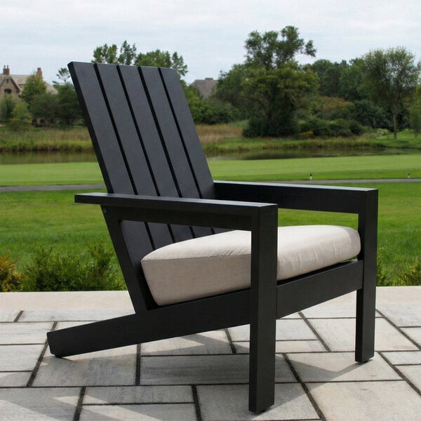 A black slatted outdoor chair with a beige cushion, placed on a tiled patio with a grassy landscape in the background.