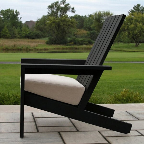 A black slatted outdoor chair with a beige cushion, positioned on a patio with a grassy landscape in the background.