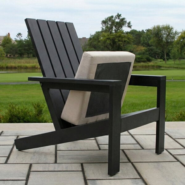 A modern black Adirondack chair with a slatted back and a light-colored cushion, placed on a patio with a grassy landscape in the background.