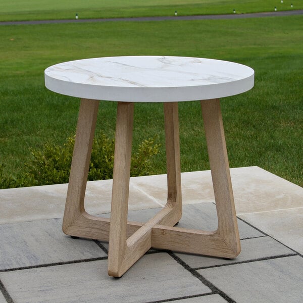 A round table with a white marble-like top and light wood legs, placed outdoors on a stone patio.