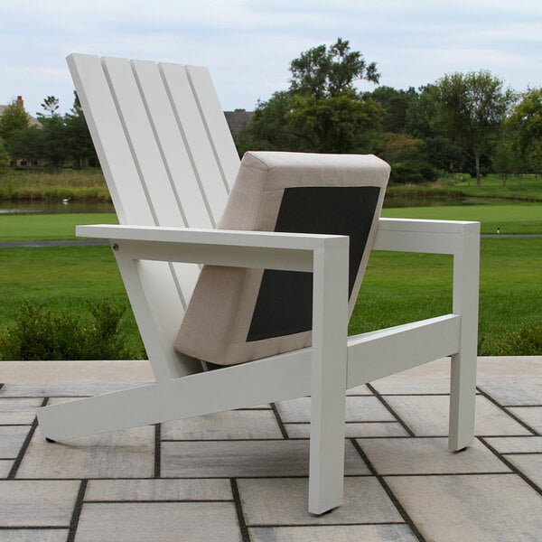A white slatted outdoor chair with a beige and black cushion, placed on a tiled patio with a grassy landscape in the background.