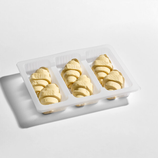 A plastic tray containing nine unbaked croissants arranged in three rows.