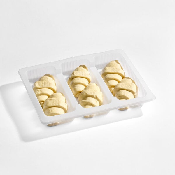 A plastic tray containing nine unbaked, crescent-shaped croissants arranged in three rows.