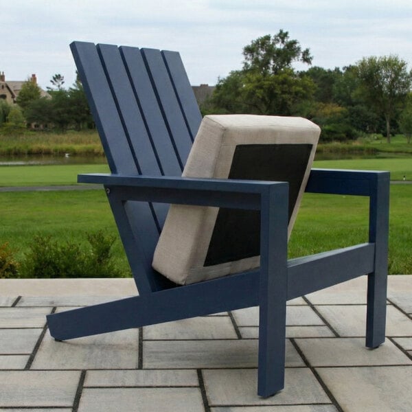 A blue Adirondack-style chair with a beige cushion is placed on a patio with a grassy landscape in the background.