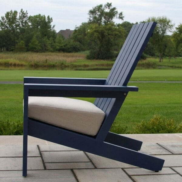 A blue outdoor chair with a slatted backrest and a light-colored cushion, placed on a patio with a grassy landscape in the background.