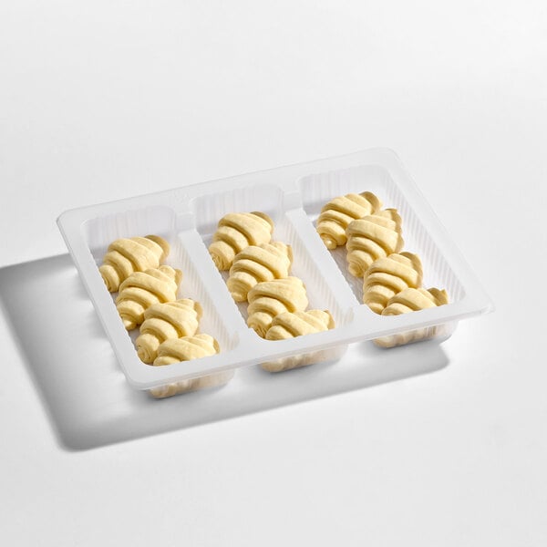 A white plastic tray containing three rows of small, unbaked, crescent-shaped pastries.