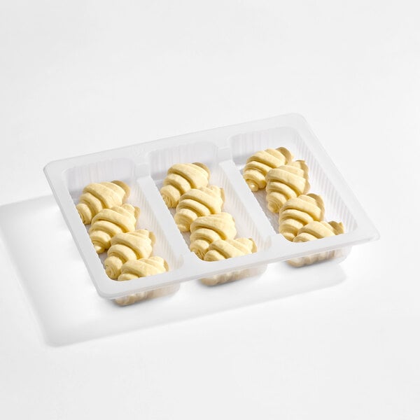 A white plastic tray containing three rows of unbaked, mini croissants arranged neatly.