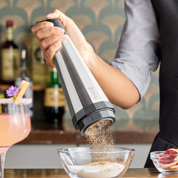 A person is using a handheld electric grinder to sprinkle ground spices into a bowl.