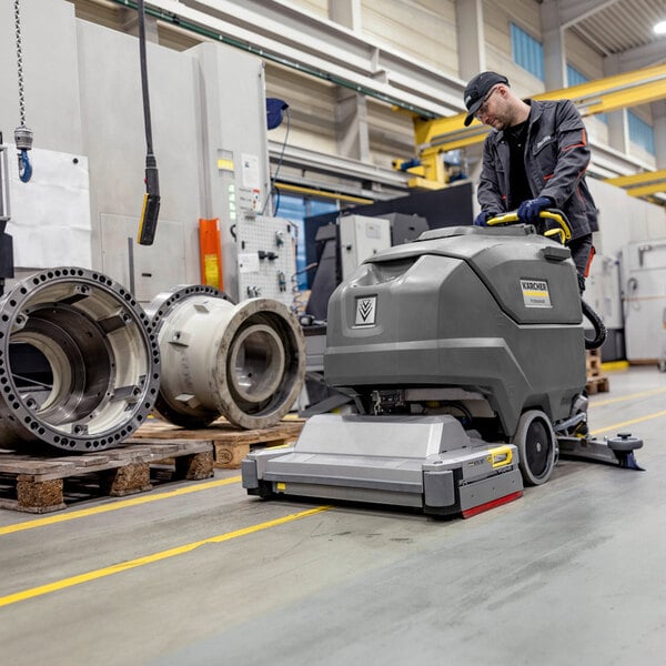 A person is operating a large, industrial floor scrubber in a factory or workshop setting.