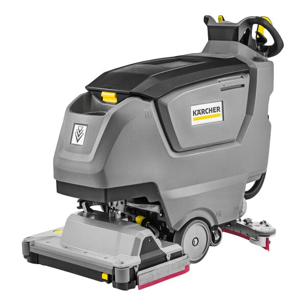 A large, gray and black walk-behind floor scrubber with wheels, a handle, and visible control panel.