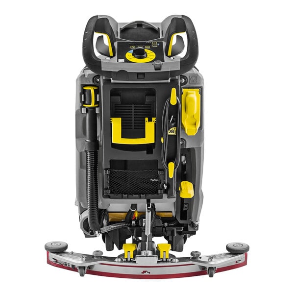 A full view of a gray and yellow walk-behind floor scrubber with visible control handles, hoses, and a curved squeegee attachment at the base.