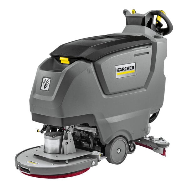 A large, gray, walk-behind floor scrubber machine with visible wheels, control handles, and a circular scrubbing pad at the front.