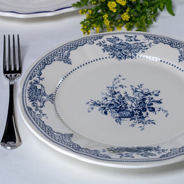 A white round plate with intricate blue floral patterns along the border and center, placed next to a fork on a white tablecloth.