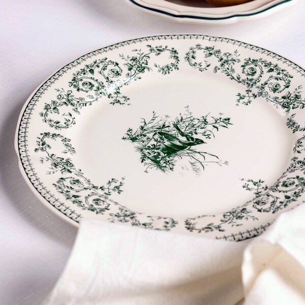 A round white plate with green floral and bird patterns along the rim and center, partially covered by a white napkin.