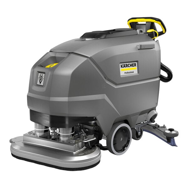 A large, gray, industrial walk-behind floor scrubber with wheels, a handle, and visible scrubbing components at the front.