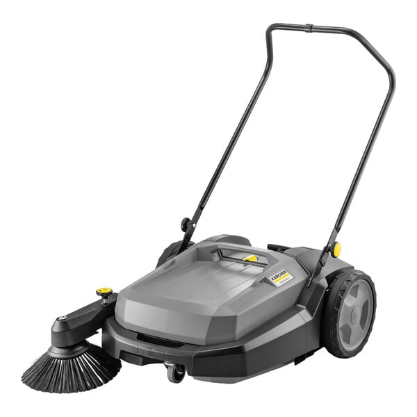 A gray walk-behind manual floor sweeper with a large handle, two wheels, and a circular side brush.