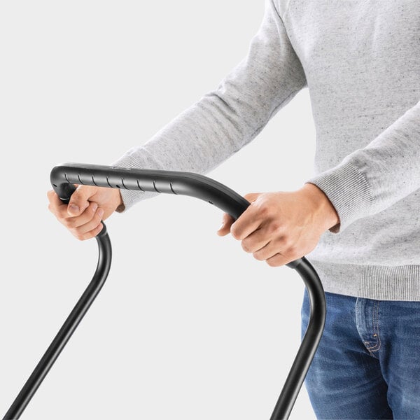 A person wearing a gray sweater and blue jeans is holding the handle of a black metal frame, possibly part of a manual push device.