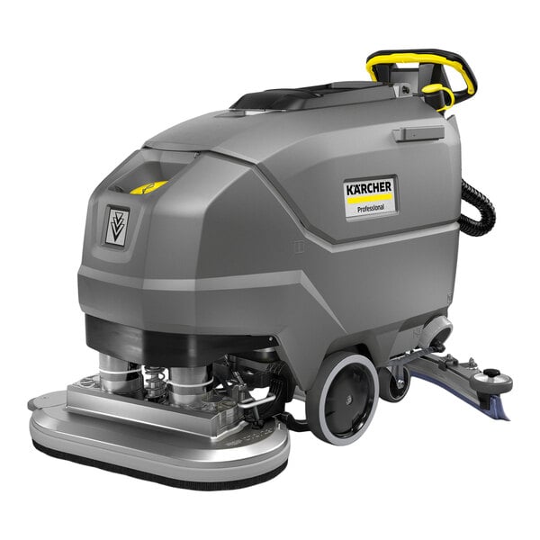 A large, gray, industrial floor scrubber with wheels, a handle, and visible cleaning components at the front.