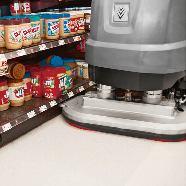 A large floor scrubber is cleaning the floor next to shelves stocked with jars of peanut butter in a grocery store.