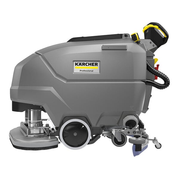 A large, gray, industrial floor scrubber with wheels, a control handle, and visible cleaning components.
