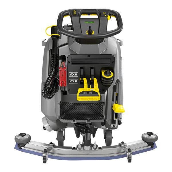 A rear view of a large, industrial walk-behind floor scrubber with a steering handle, control panel, hoses, and various levers and attachments visible.