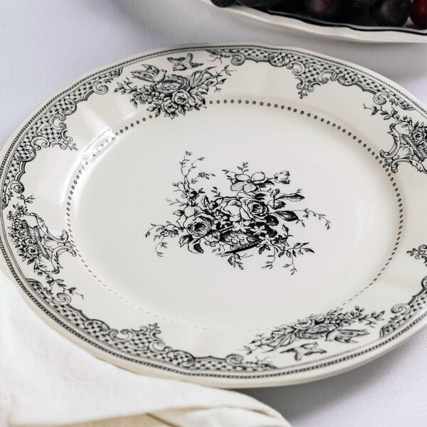 A round white plate with intricate black floral patterns along the rim and a floral bouquet design in the center.