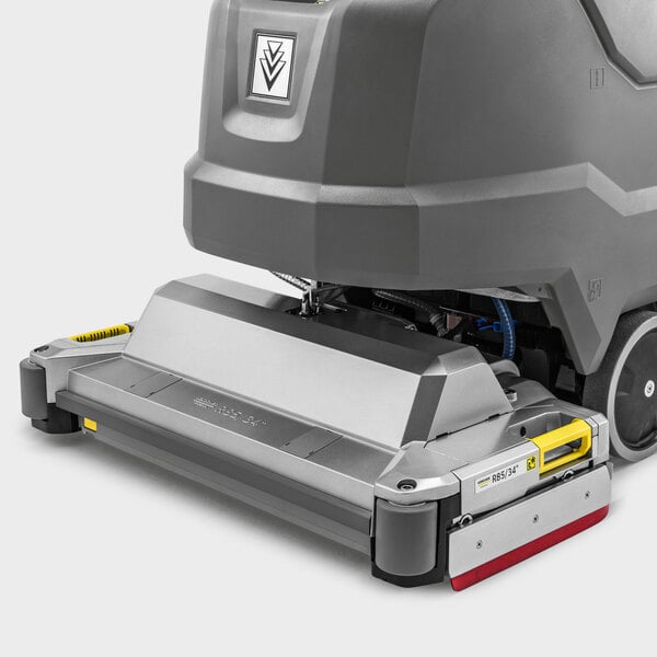 A partial view of a large, gray and metallic floor cleaning machine with wheels and a rectangular scrubbing head.