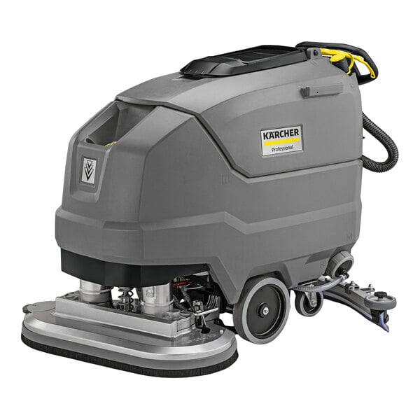 A large, gray, industrial walk-behind floor scrubber with wheels, a control handle, and visible cleaning components at the base.