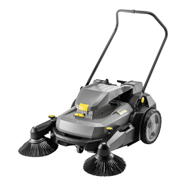 A gray walk-behind floor sweeper with two large side brushes, a handlebar, and large rear wheels.