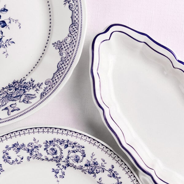 Three white plates with blue decorative patterns and scalloped edges are arranged on a light textured surface; two plates feature intricate floral designs, while one has a simple blue border.