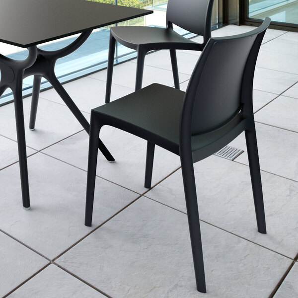 A modern black chair with a curved backrest and four straight legs, placed next to a matching table on a tiled floor.