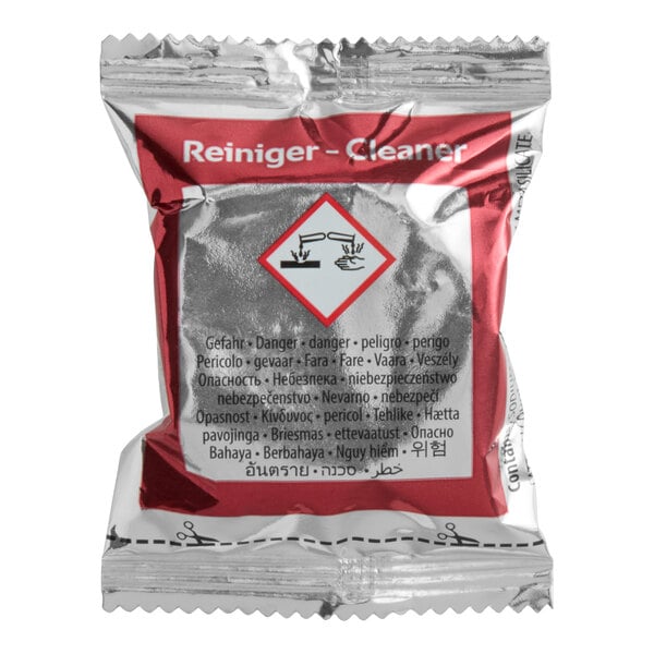 A sealed, metallic packet labeled 'Reiniger - Cleaner' with a hazard symbol and multilingual warnings, indicating it contains a chemical cleaning tablet.