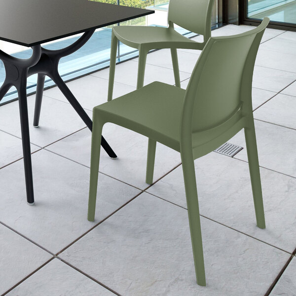 Two olive green chairs with a modern design are placed next to a black table on a tiled floor in a bright indoor or outdoor setting.