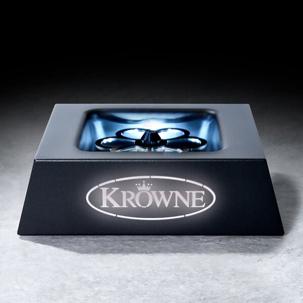 A black, square-shaped tabletop device with a metallic interior and a circular component in the center, featuring the illuminated brand name 'Krowne' on the front.