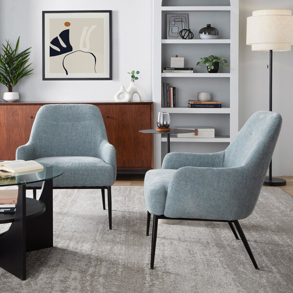 Two light blue upholstered accent chairs with black metal legs are positioned in a modern living room with a gray rug, wooden sideboard, and minimalist decor.