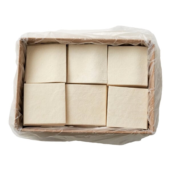 Six square, pale dough sheets are arranged in a cardboard box lined with plastic.
