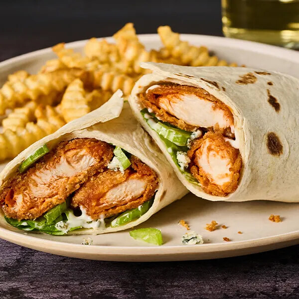 A plate with a wrap filled with breaded chicken, lettuce, and sauce, served with crinkle-cut fries.