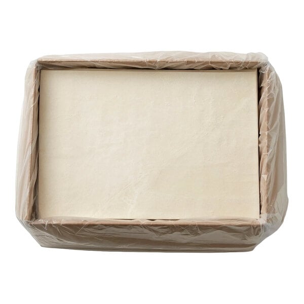A rectangular block of pale dough wrapped in plastic and placed inside a cardboard box.