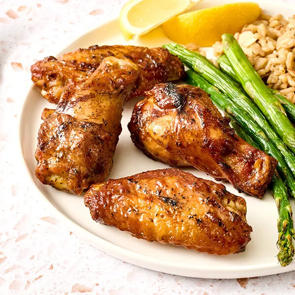 A plate with four grilled chicken wings, asparagus spears, a grain side, and lemon wedges.